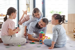 A father with three daughters indoors at home, playing on floor.