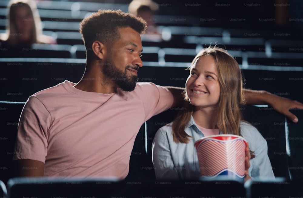 A front view of cheerful young couple in love in the cinema, watching film.