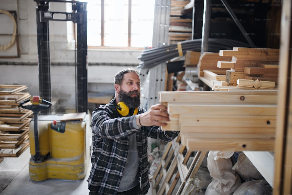 Falegname maschio maturo con una tavola di legno all'interno in un laboratorio di falegnameria. Concetto di piccola impresa.