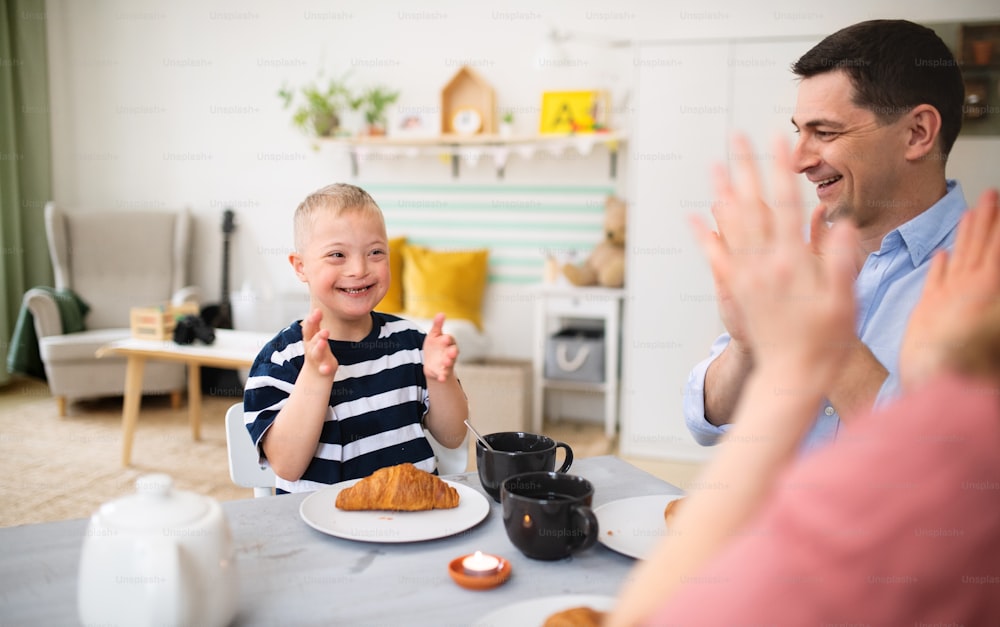 A happy family with down syndrome son at the table, clapping when having breakfast.