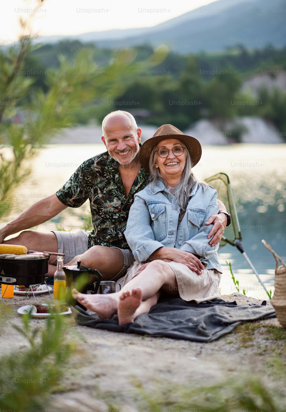 Portrait of happy senior couple resting on summer holiday trip, barbecue by lake.