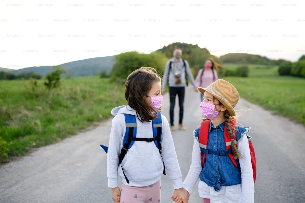 Front view of family with two small daughters on trip outdoors in nature, wearing face masks.