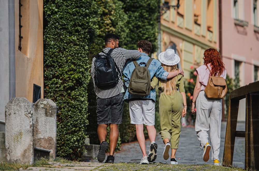 Uma visão traseira de um grupo de jovens felizes ao ar livre em viagem na cidade, andando de braços dados.