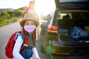 Front view of small girl with family on trip outdoors in nature, wearing face masks.
