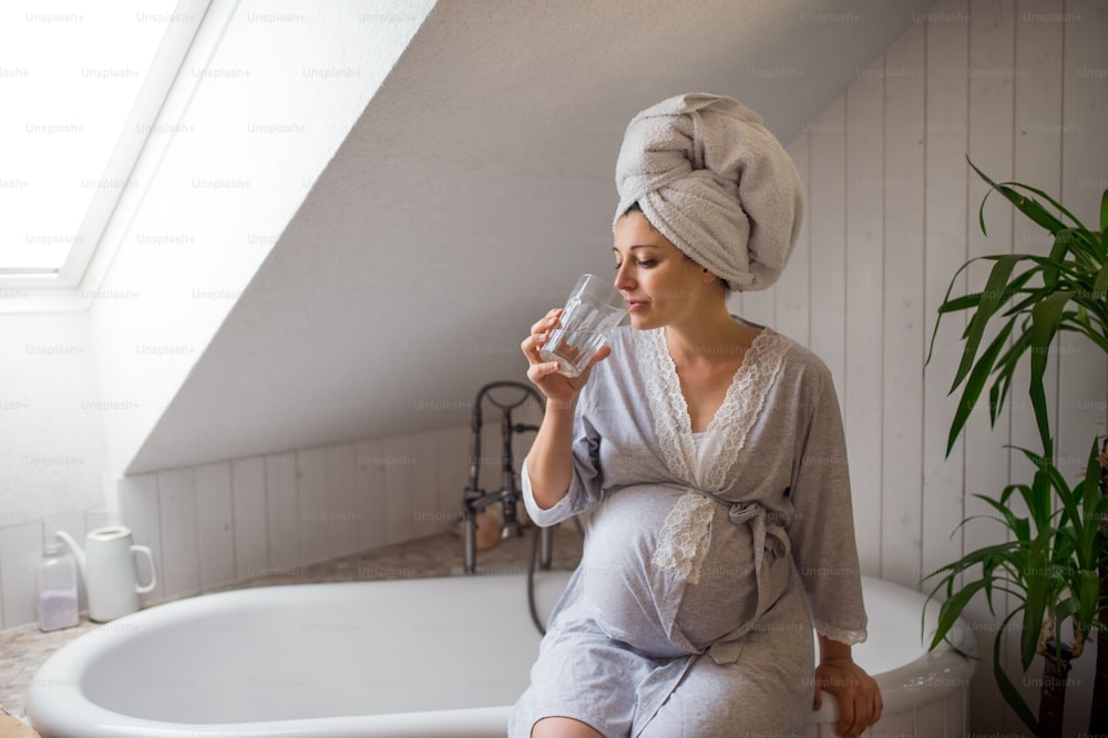 Portrait d’une femme enceinte heureuse à l’intérieur dans la salle de bain à la maison, eau potable.