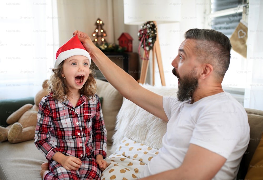 Portrait d’un père avec sa petite fille à l’intérieur à la maison à Noël, s’amusant.