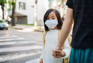 Portrait of small Japanese girl with mother walking outdoors in town, coronavirus concept. Copy space.