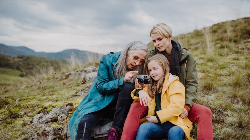 A small girl with mother and grandmother taking pictures on top of mountain in autumn day.