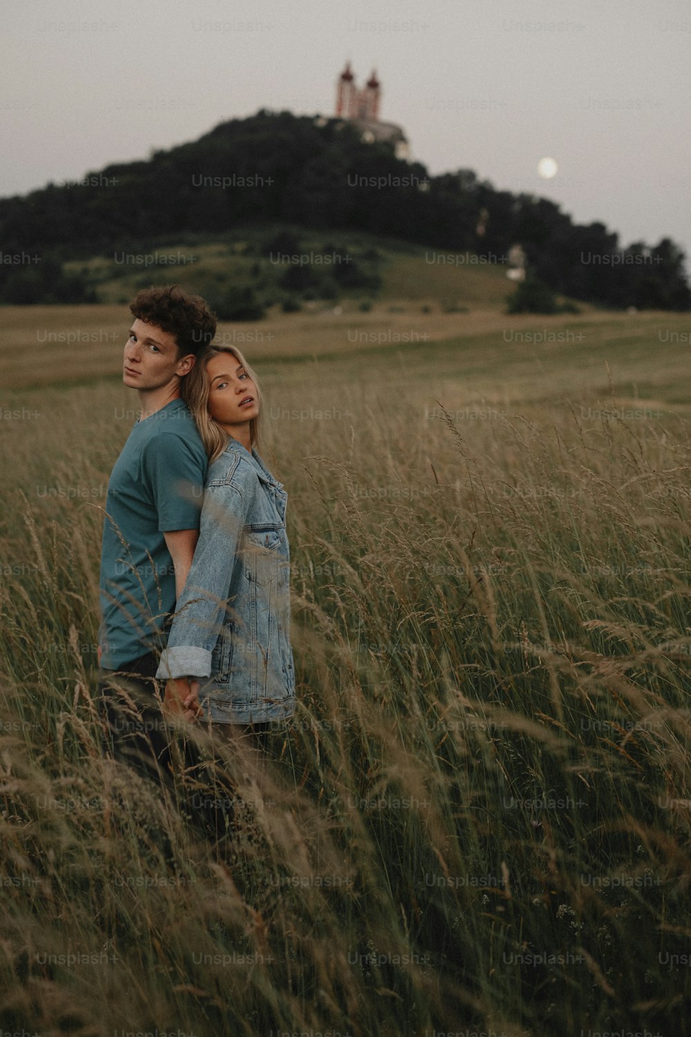 Una pareja joven en un paseo por la naturaleza al atardecer en el campo, de pie espalda con espalda y mirando a la cámara.