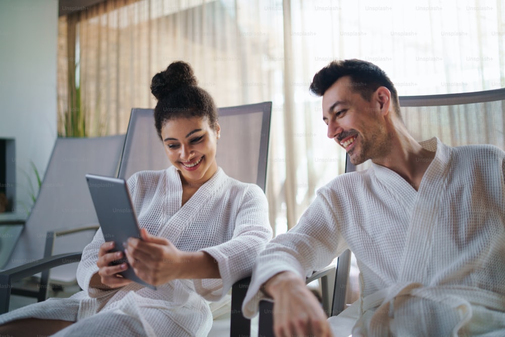 A portrait of young couple relaxing in spa resort, using tablet.