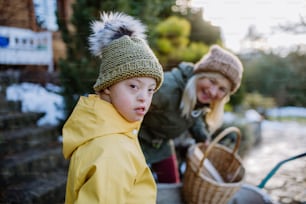 Un niño con síndrome de Down mirando a la cámara y trabajando en el jardín en invierno con su abuela.