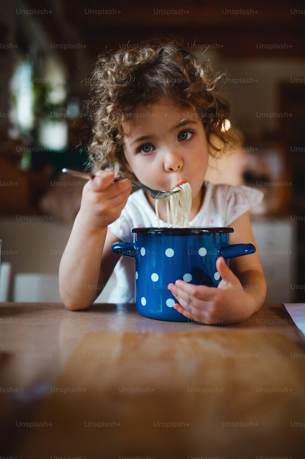 Retrato de una niña triste sentada en la mesa en el interior de la casa, comiendo espaguetis.