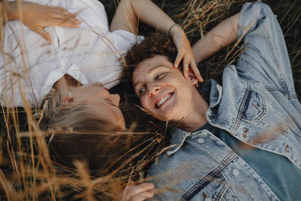A top view of young couple on a walk in nature in countryside, lying in long grass.