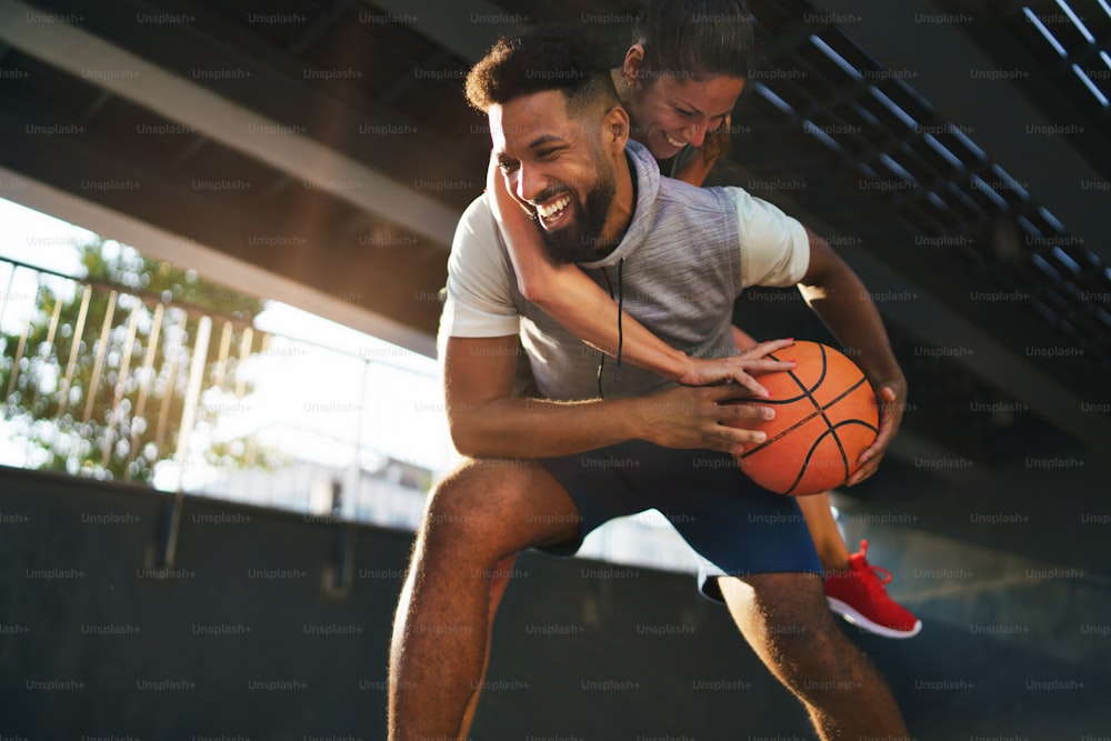 Um homem e uma mulher amigos jogando basquete ao ar livre na cidade, se divertindo.