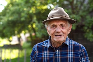 Un ritratto di uomo anziano in piedi all'aperto in giardino, guardando la macchina fotografica.