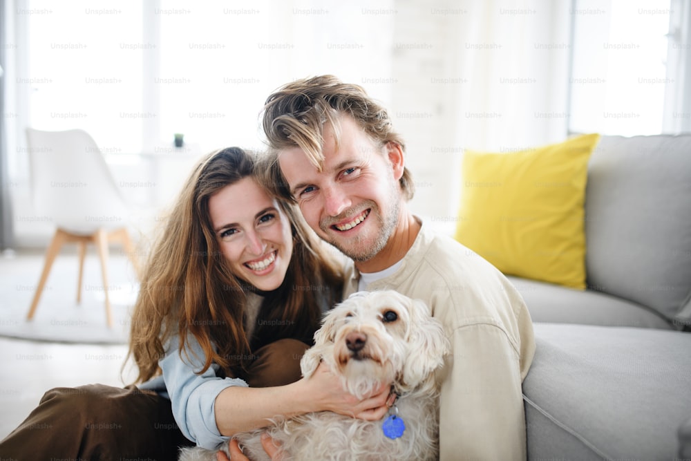 A happy young couple in love with dog indoors at home, looking at camera.