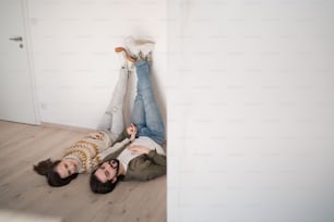 A young couple lying on floor and moving in new flat, looking at camera.