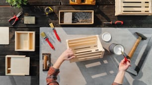 Top view of unrecognizable woman making and painting wooden boxes, small business and desktop concept.