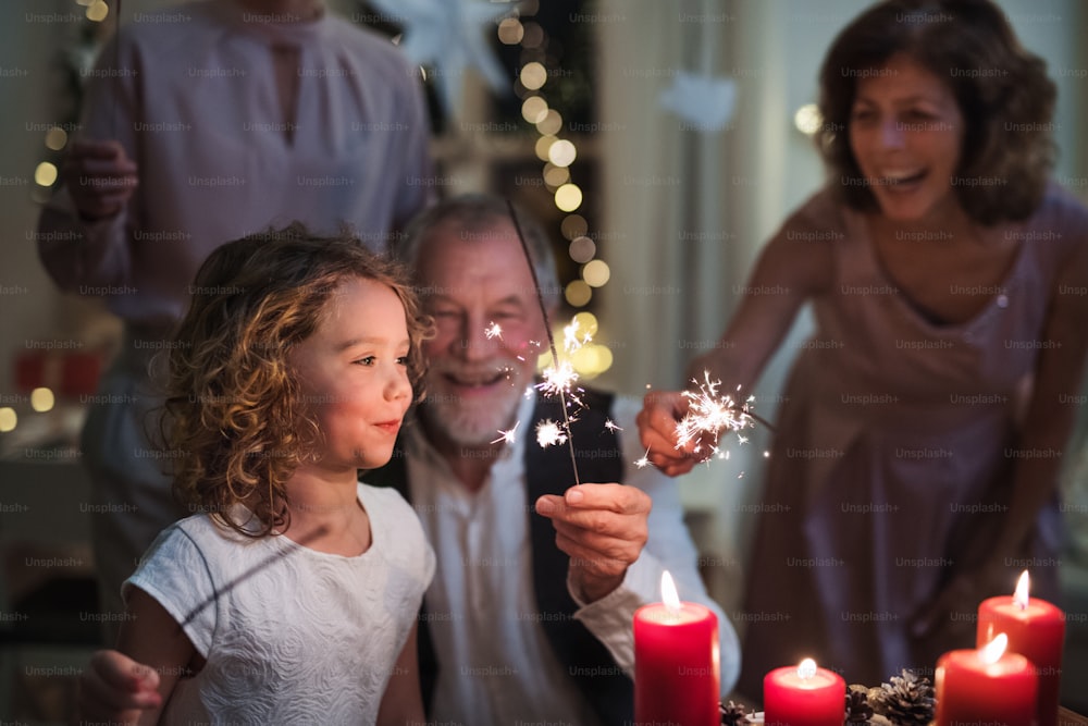 Petite fille avec ses parents et ses grands-parents à l’intérieur pour célébrer Noël, tenant des cierges magiques.