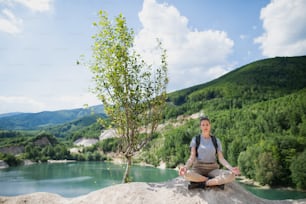 A mid adult woman tourist on hiking trip on summer holiday, doing yoga and meditating.