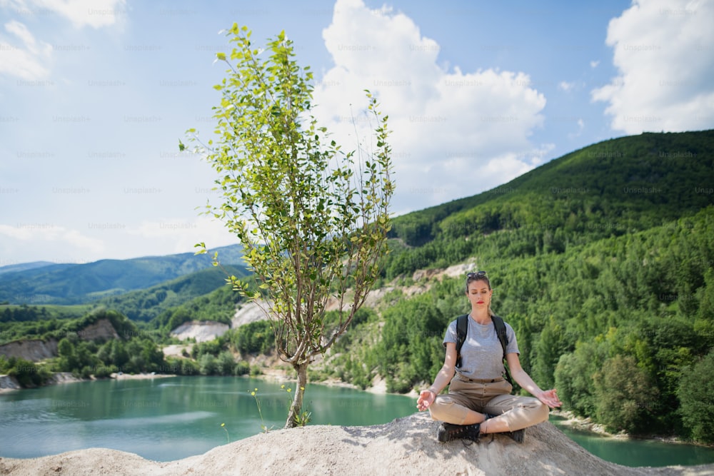 A mid adult woman tourist on hiking trip on summer holiday, doing yoga and meditating.