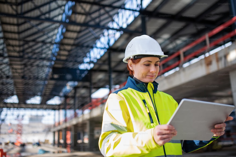 Una mujer ingeniera con una tableta de pie en un sitio de construcción, trabajando. Espacio de copia.