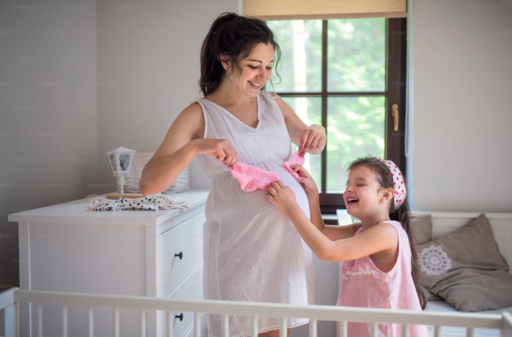 Ritratto di donna incinta con figlia piccola all'interno di casa, divertendosi.