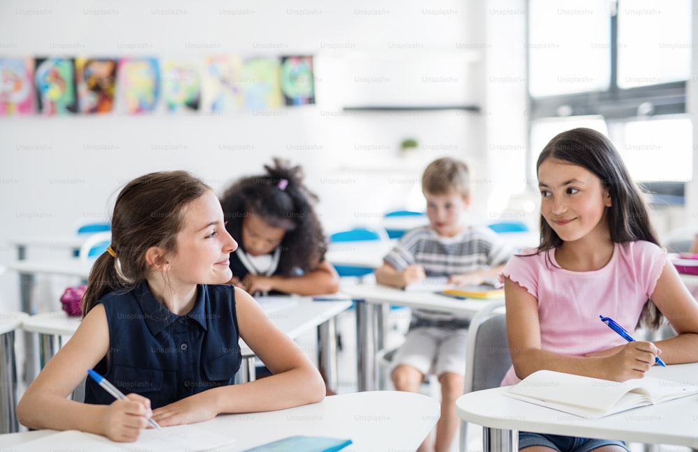 Pequenas crianças em idade escolar sentadas na mesa da sala de aula na lição, conversando.