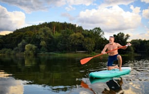Front view of senior man paddleboarding on lake in summer. Copy space.