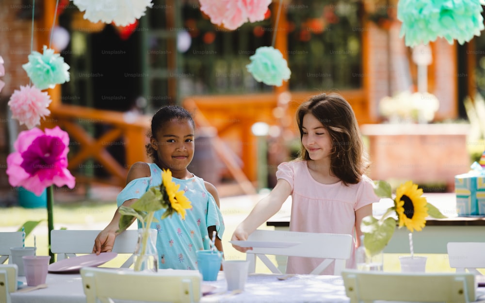 Happy small girls setting table for summer garden party, birthday celebration concept.