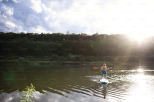 Front view of senior man paddleboarding on lake in summer. Copy space.