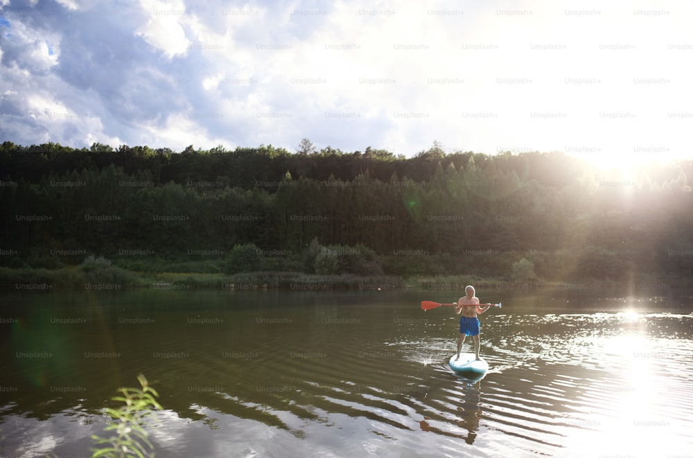 Vista frontale dell'uomo anziano paddleboarding sul lago in estate. Copia spazio.