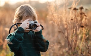 Small girl in autumn nature, taking photographs with camera. Copy space.