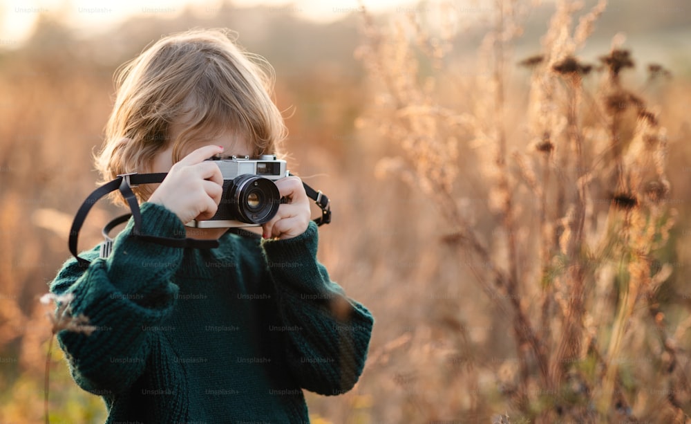 Small girl in autumn nature, taking photographs with camera. Copy space.