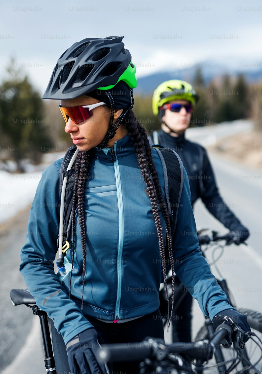 Two mountain bikers standing on road outdoors in winter, resting.