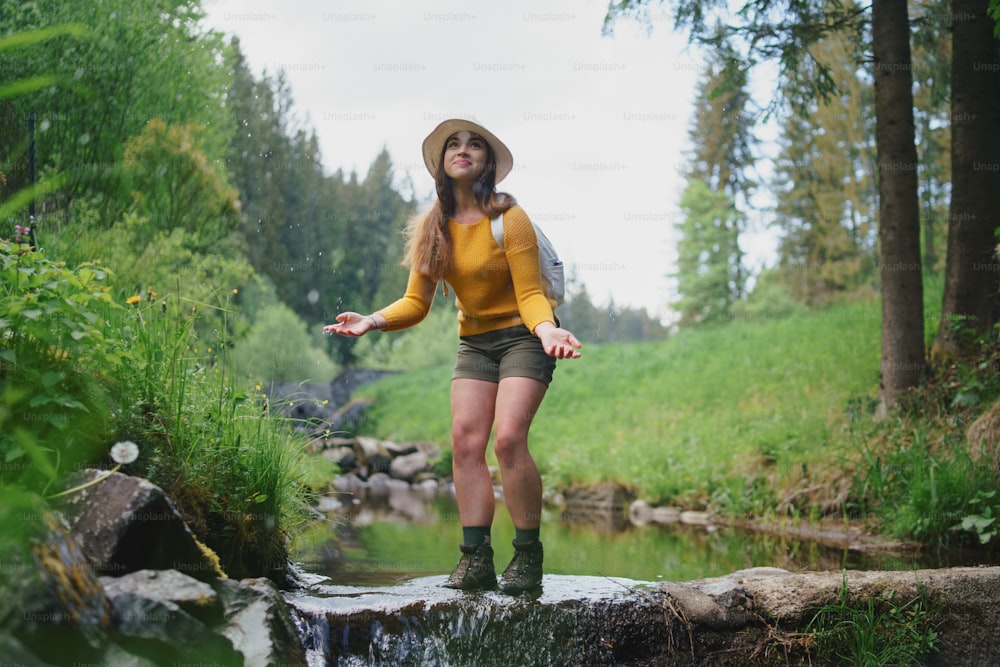 Mulher jovem feliz de pé junto ao riacho em uma caminhada ao ar livre na natureza de verão, olhando para cima.
