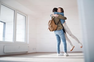 Felices propietarios de parejas jóvenes que se abrazan en un nuevo piso, se mudan, un nuevo hogar y un concepto de reubicación.