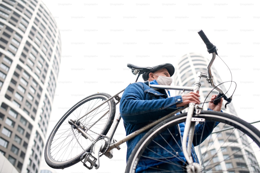 Un hombre mayor que lleva una bicicleta al aire libre en la calle de la ciudad, concepto de coronavirus.