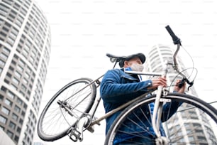 A senior man carrying bicycle outdoors on street in city, coronavirus concept.