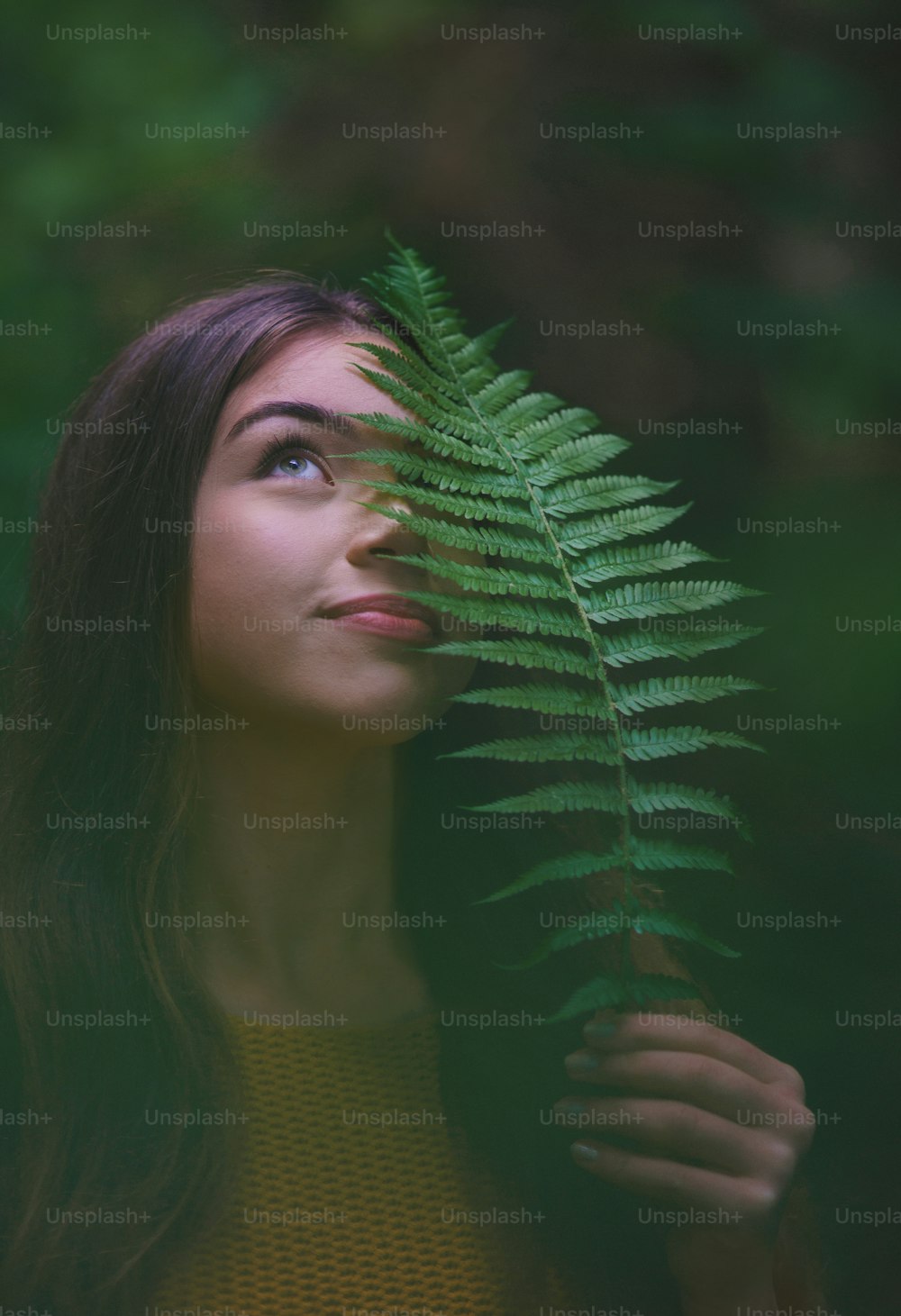 Close-up portrait of young woman on a walk outdoors in forest in summer nature, holding fern.