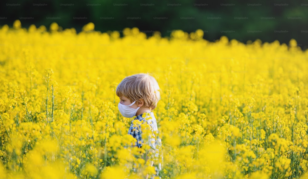 Side view of happy small boy standing in spring nature in rapeseed field.
