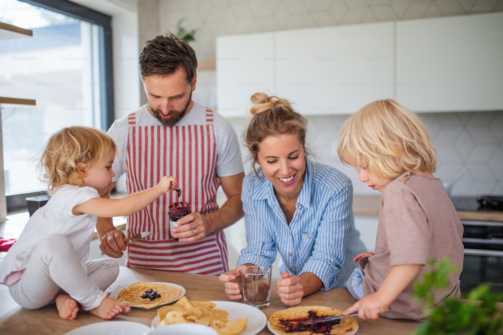 Vista frontal de una familia joven con dos niños pequeños en el interior de la cocina, comiendo panqueques.