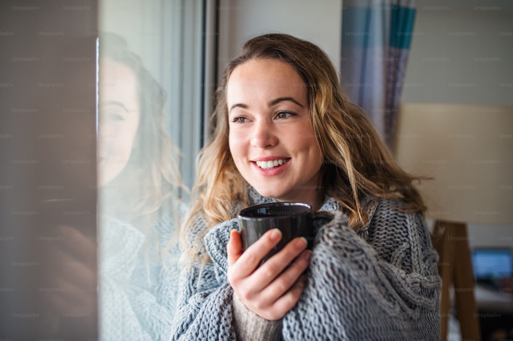 Front view of young woman relaxing indoors at home with cup of coffee or tea.