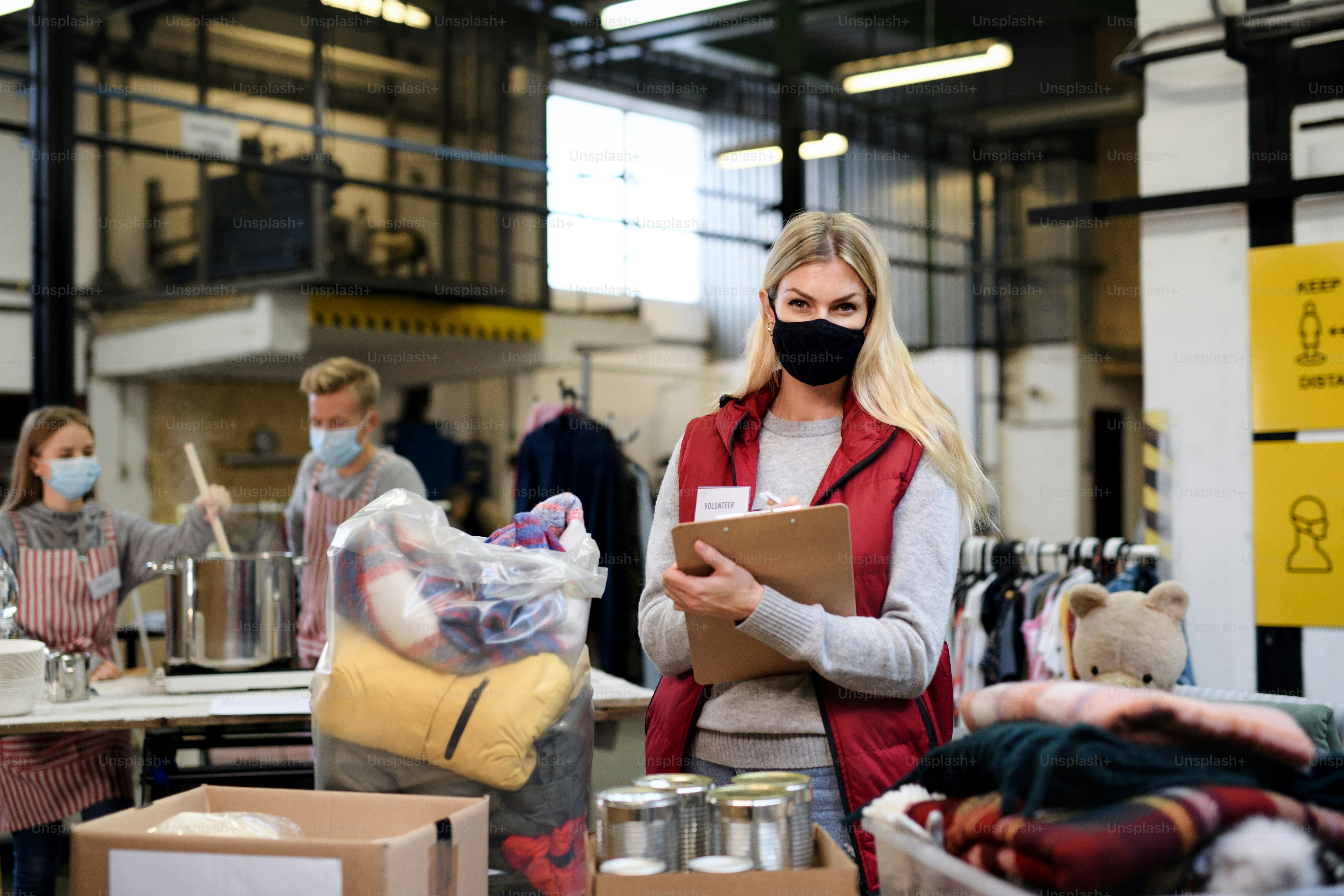 Woman volunteer working with food and clothes in community charity donations center, coronavirus concept.