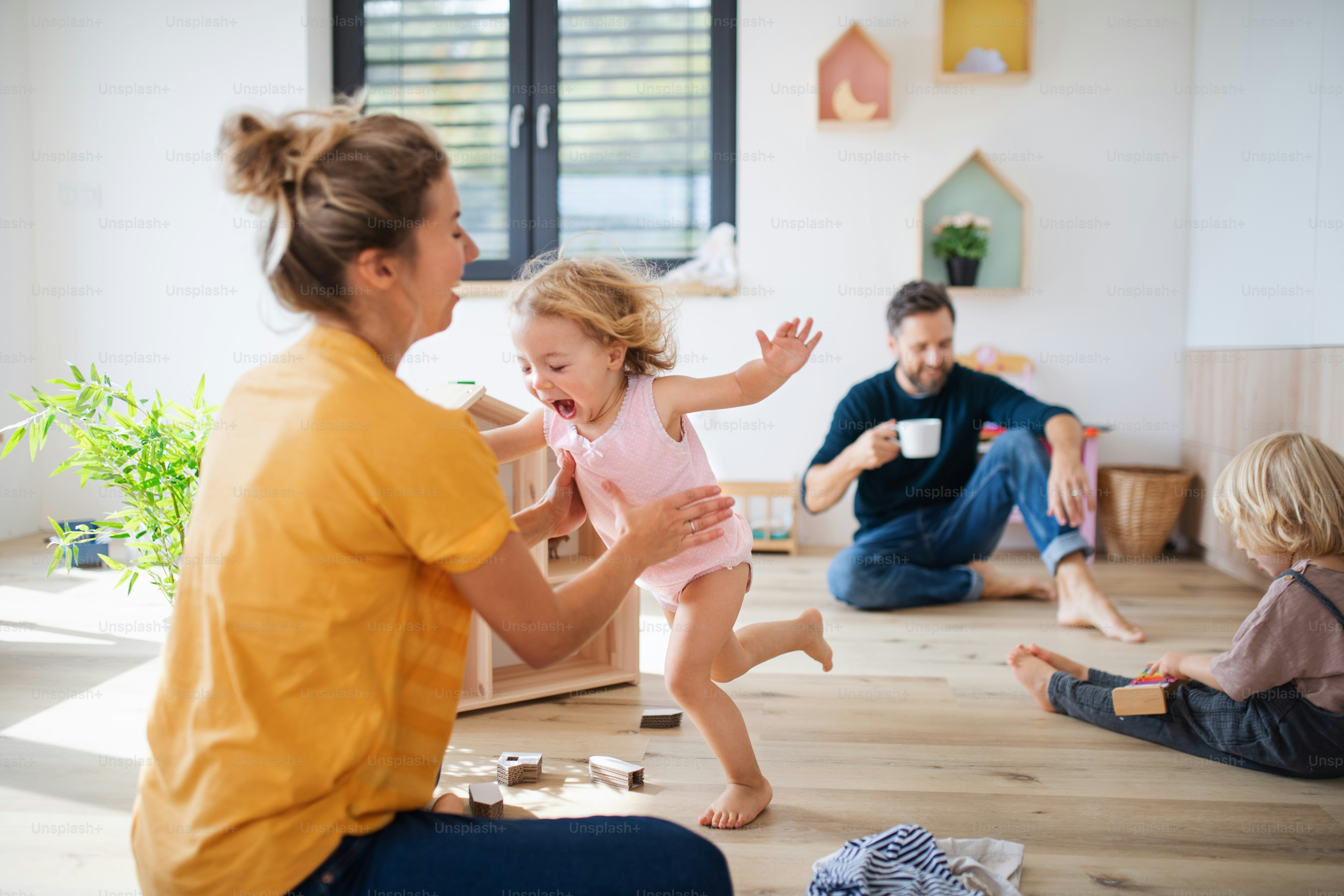 Junge Familie mit zwei kleinen Kindern drinnen im Schlafzimmer, spielend.