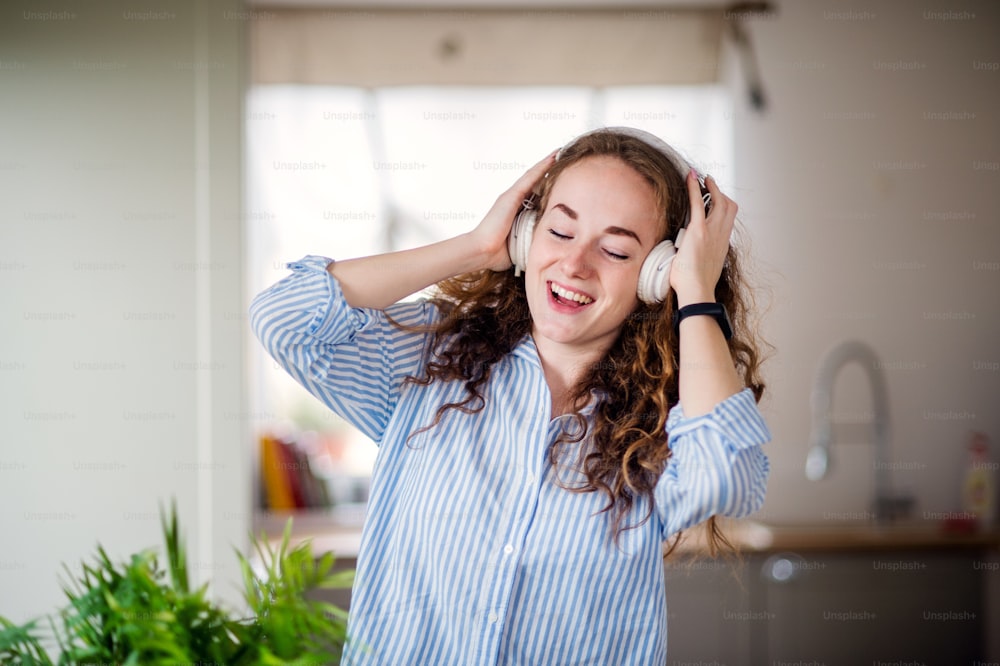 Junge Frau mit Kopfhörern entspannt sich drinnen zu Hause, hört Musik und singt.