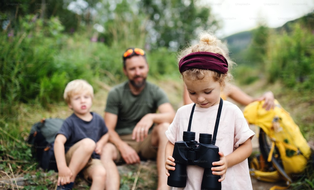 Front view of family with small children hiking outdoors in summer nature, sitting and resting.