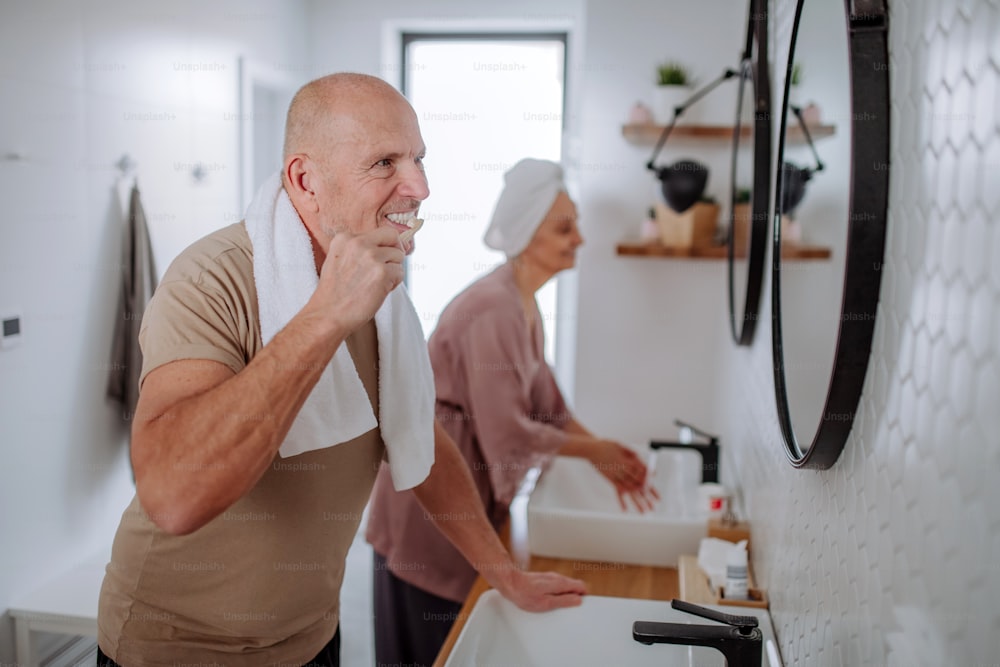 Una pareja de ancianos en el baño, cepillándose los dientes y lavándose, concepto de rutina matutina.