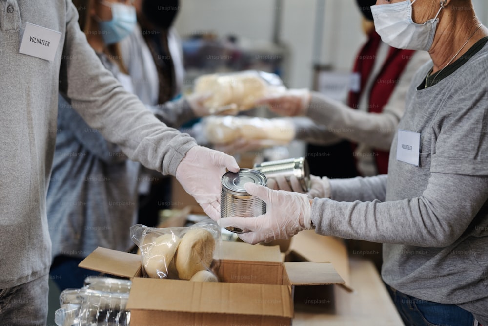 Groupe de bénévoles méconnaissables travaillant dans un centre de dons de charité communautaire, une banque alimentaire et un concept de coronavirus.