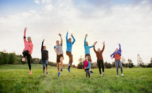 A large group of active multi generation people running a race competition in nature, jumping.